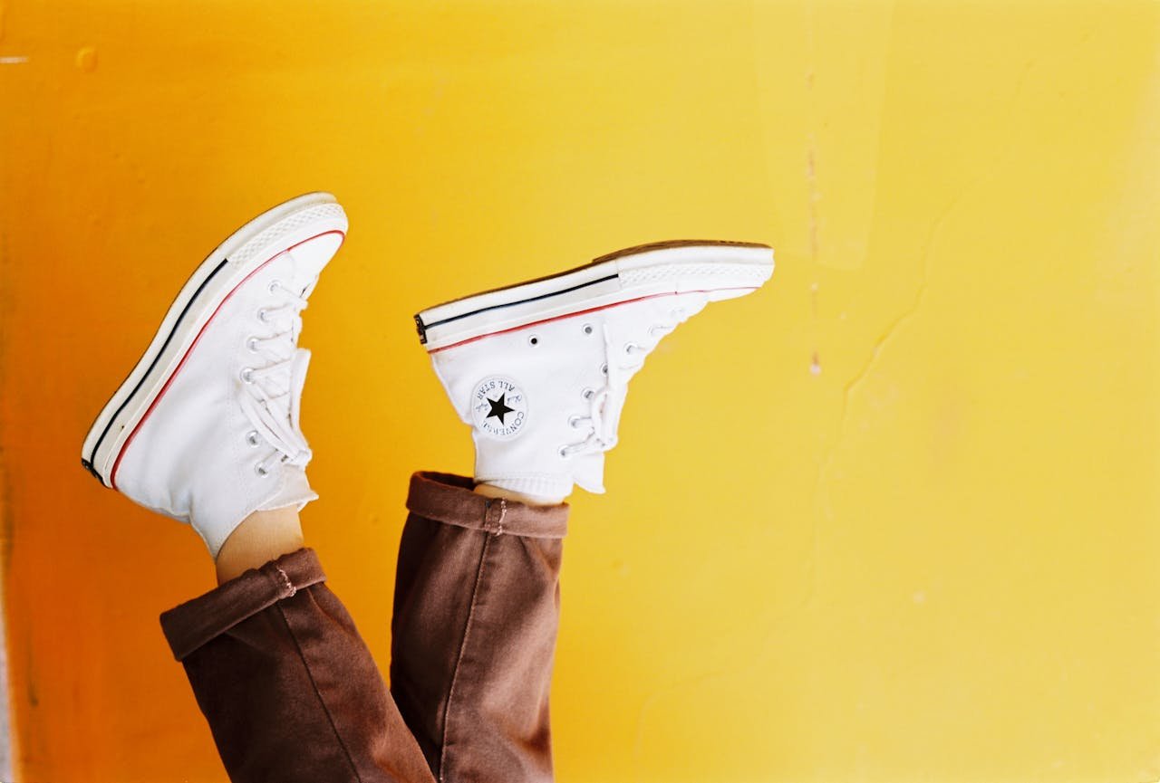 who-we-are Upside down image of white sneakers against a vibrant yellow background, showcasing trendy footwear style.